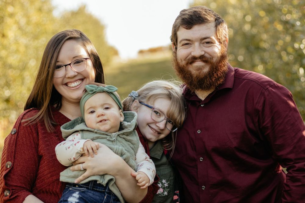A family in burgundy outfits poses together outdoors during an autumn photoshoot.