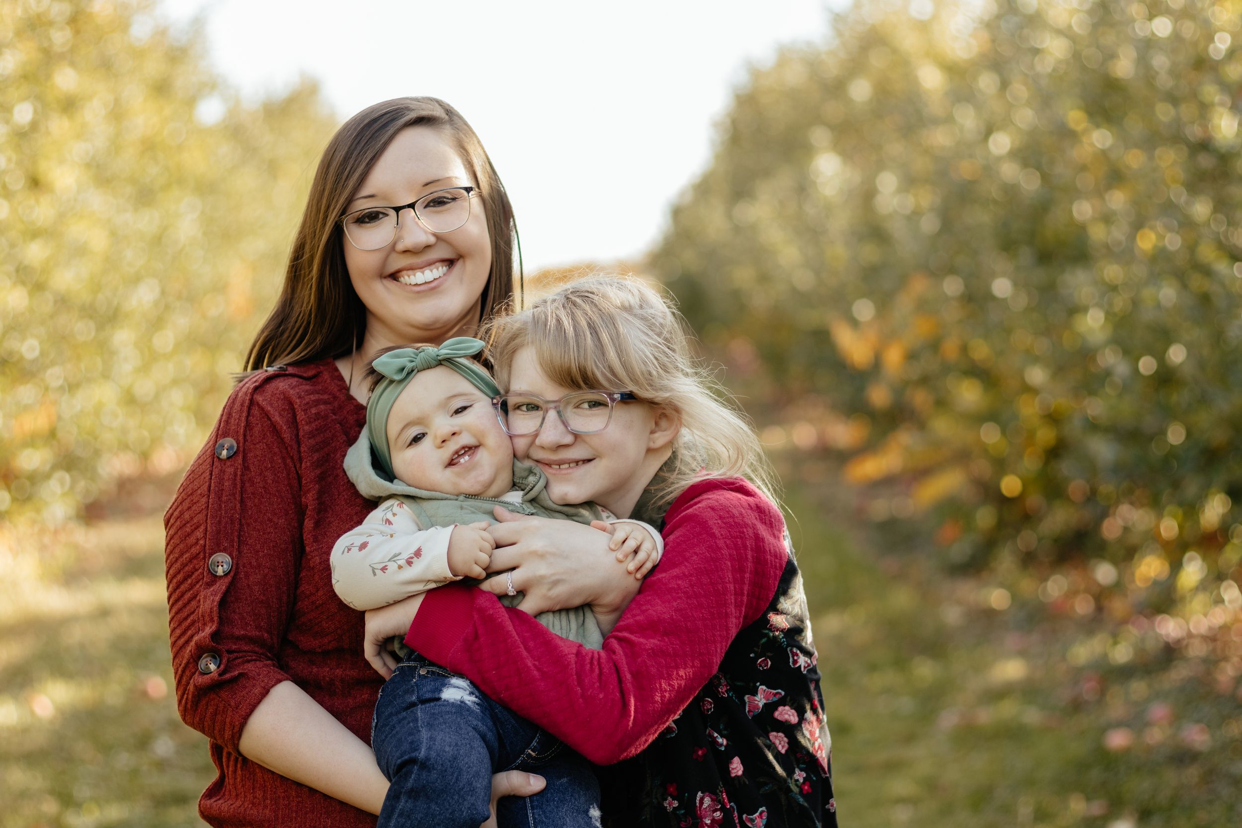 A sweet family moment captured outdoors with golden fall foliage in the background.