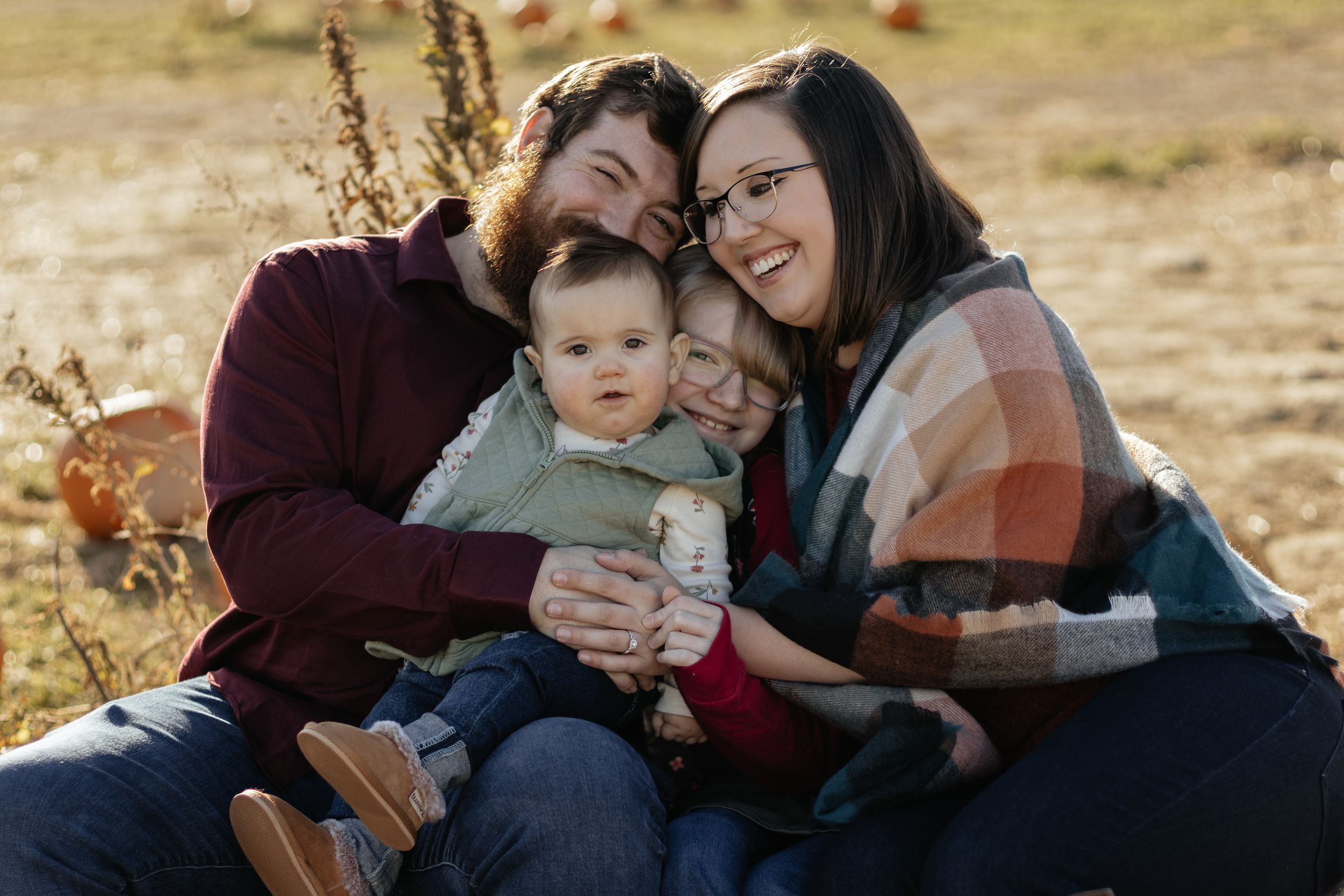 A loving family moment captured in warm sunlight against a natural outdoor backdrop.