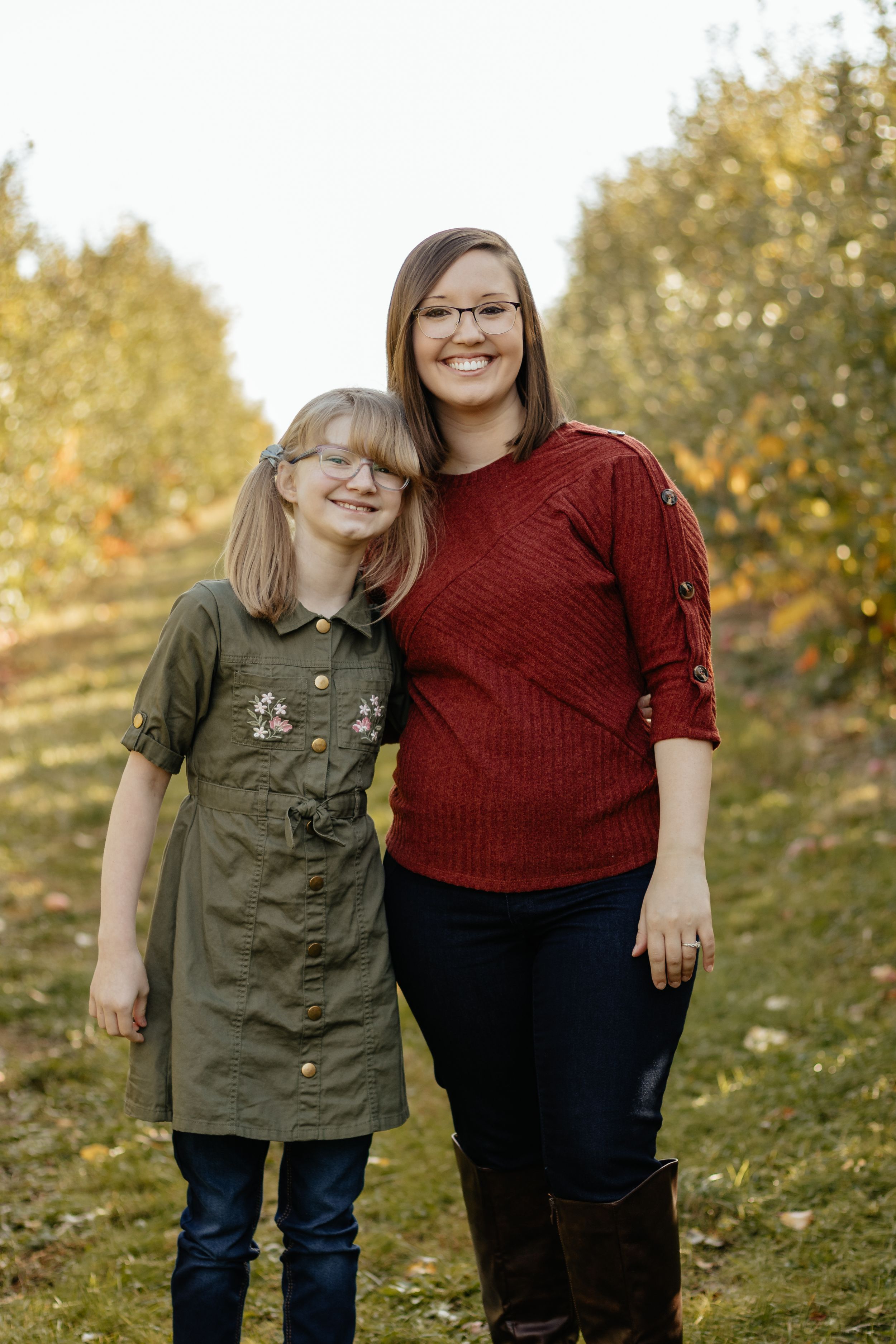 Two people in casual attire pose together on a grassy hillside during fall.
