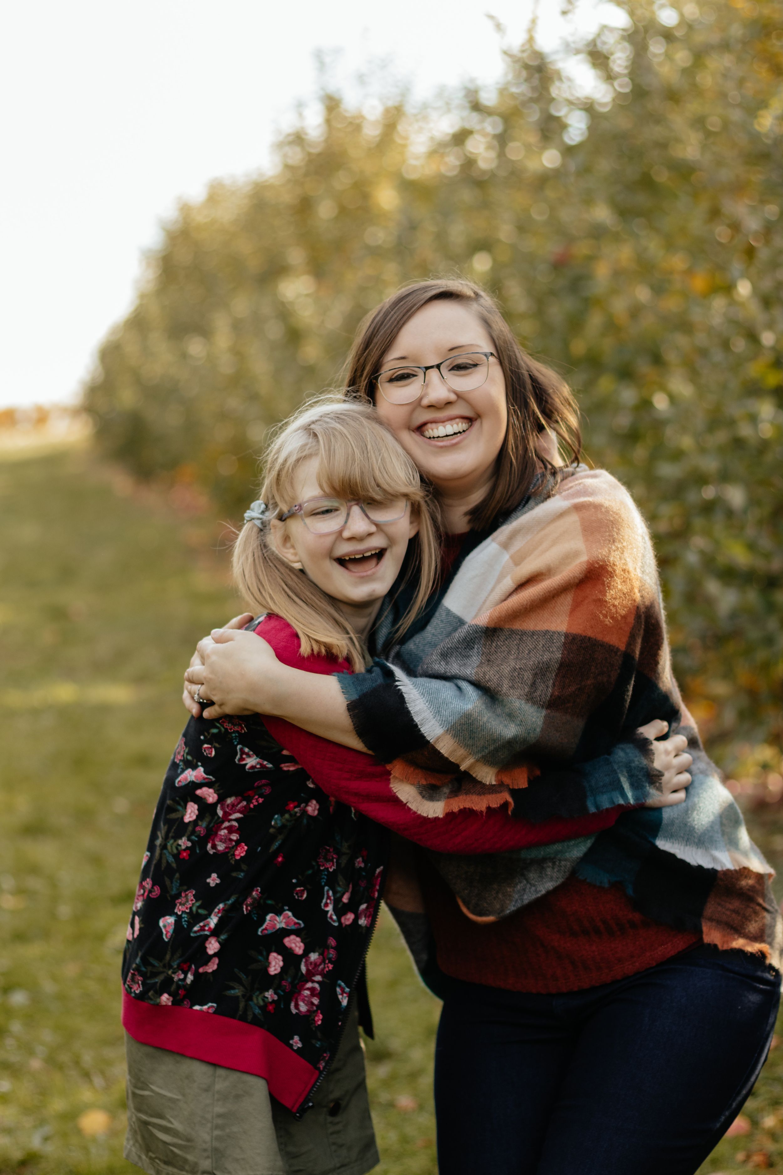 Friends laughing and hugging together in a fall orchard setting.