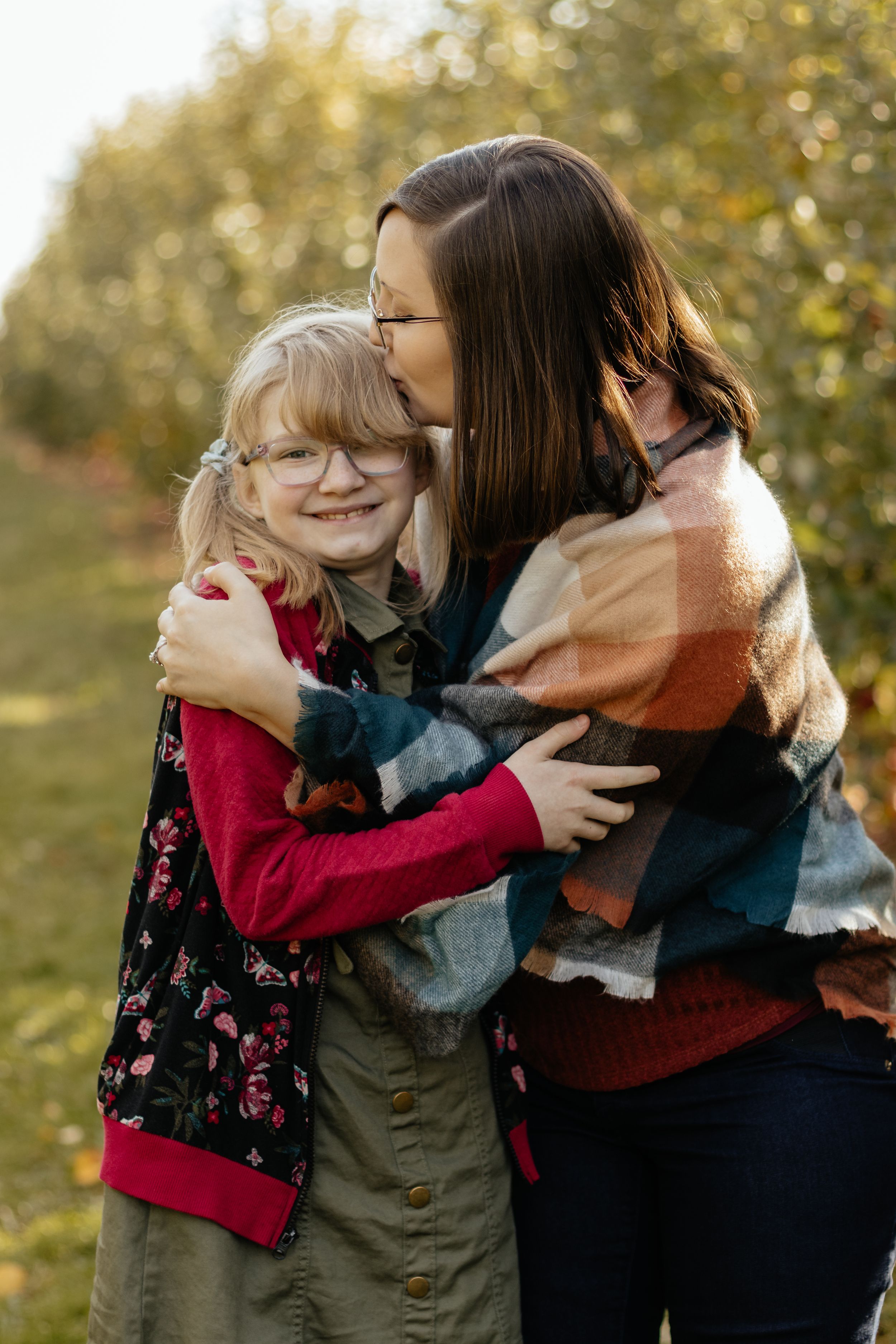 Family sharing tender hugs and embraces outdoors during autumn photoshoot with golden bokeh background.