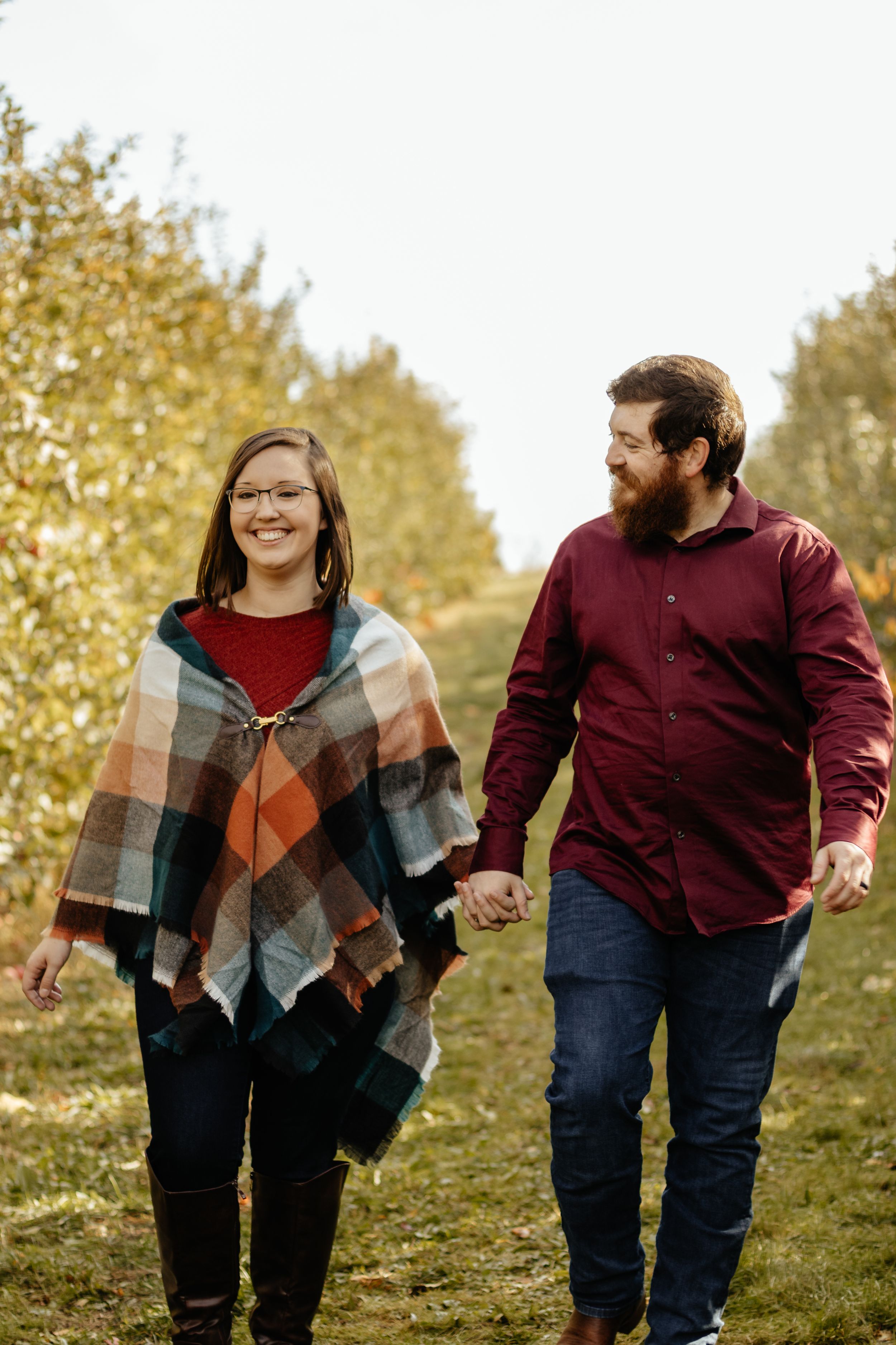Couple walking and laughing together on grassy hillside during fall photo session.