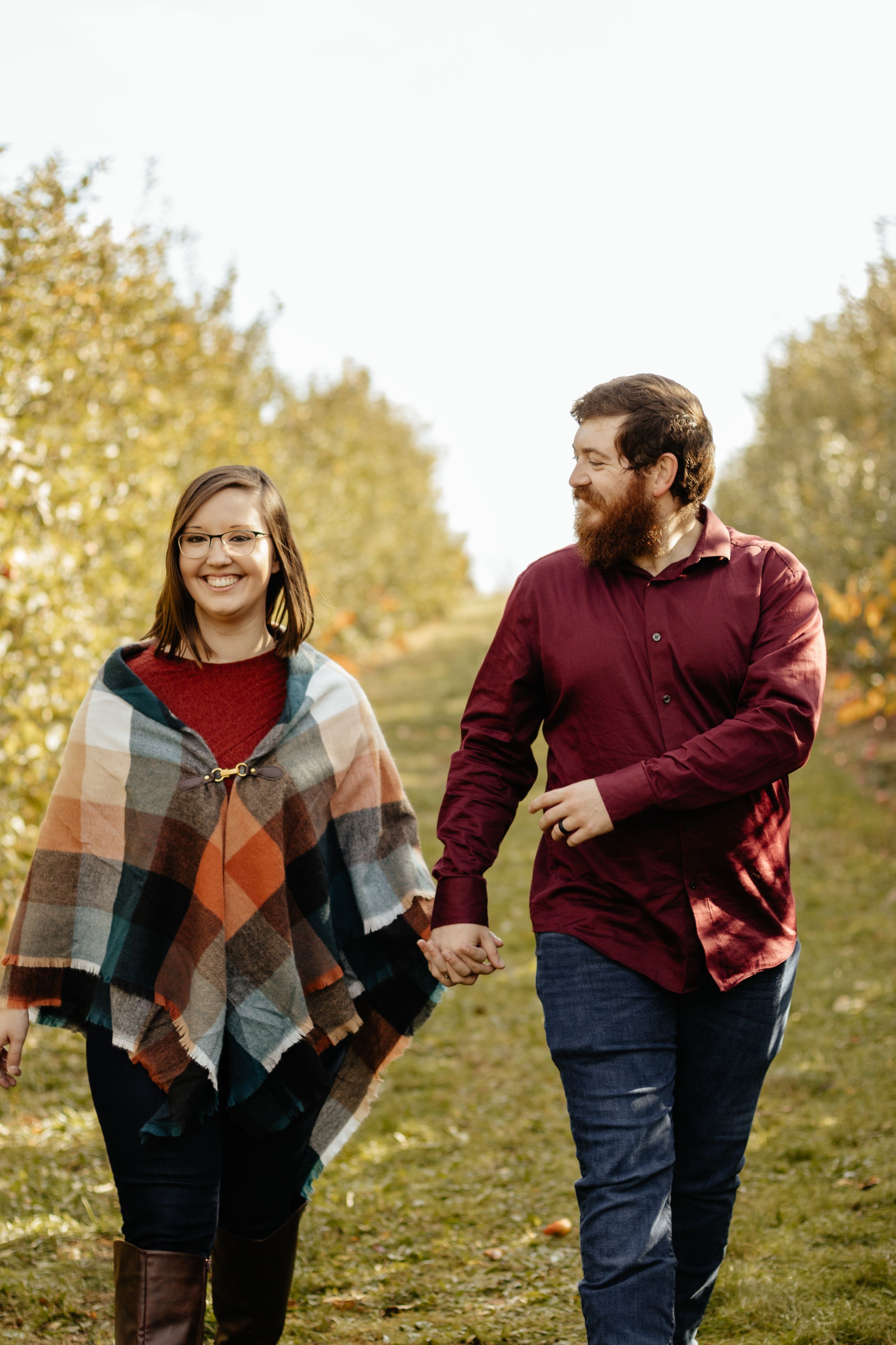 Playful couple holding hands while walking uphill during autumn photoshoot.