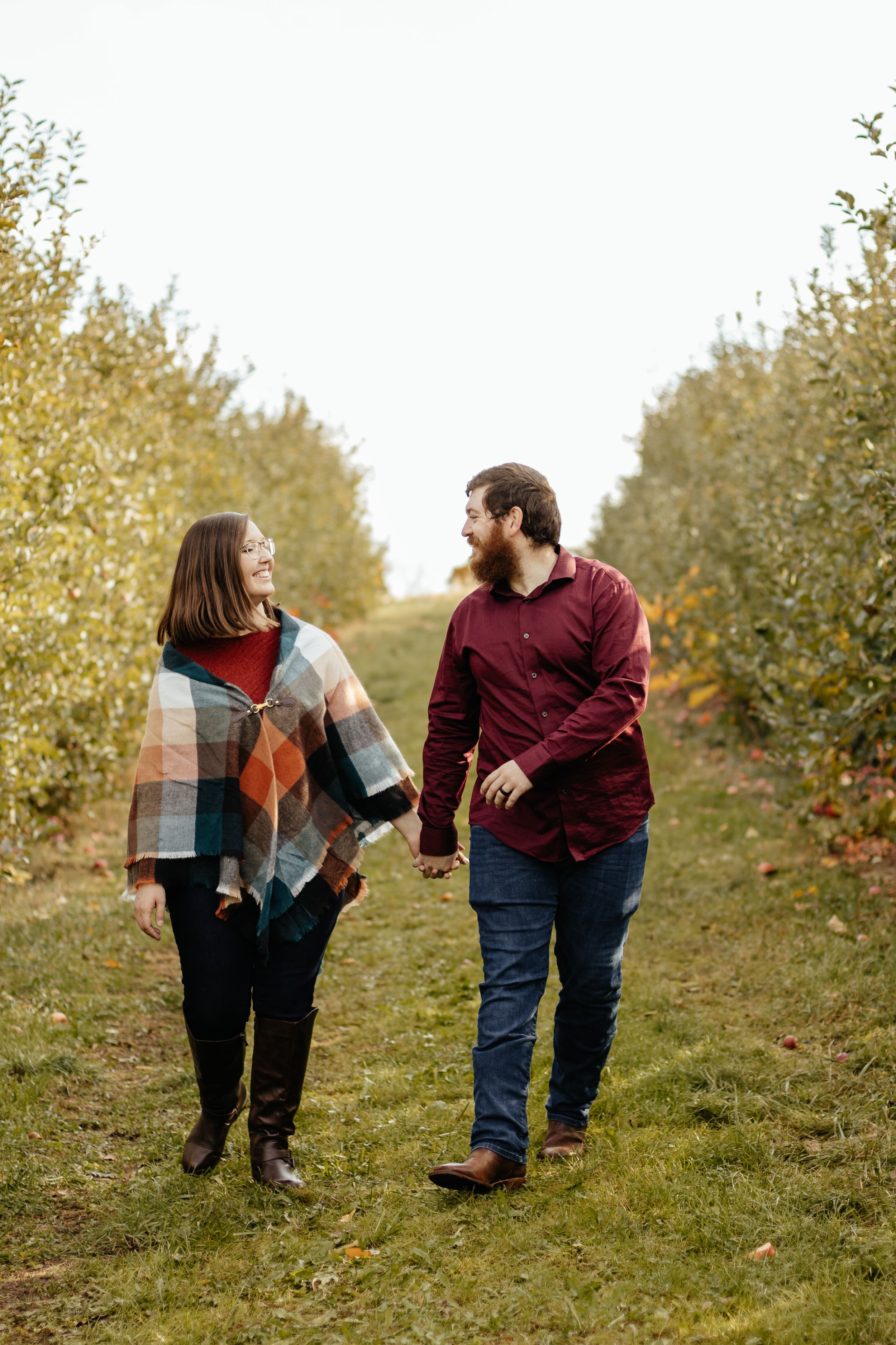 Couple walking together up grassy hill during fall outdoor photo session.