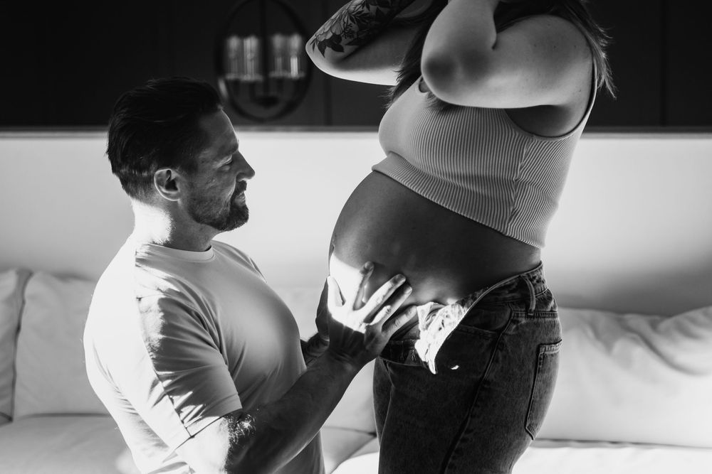 Intimate maternity photoshoot in black and white showing couple's silhouettes.