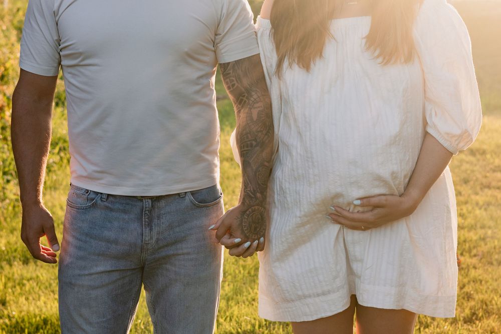 Couple holding hands during sunset maternity photoshoot in a grassy field.