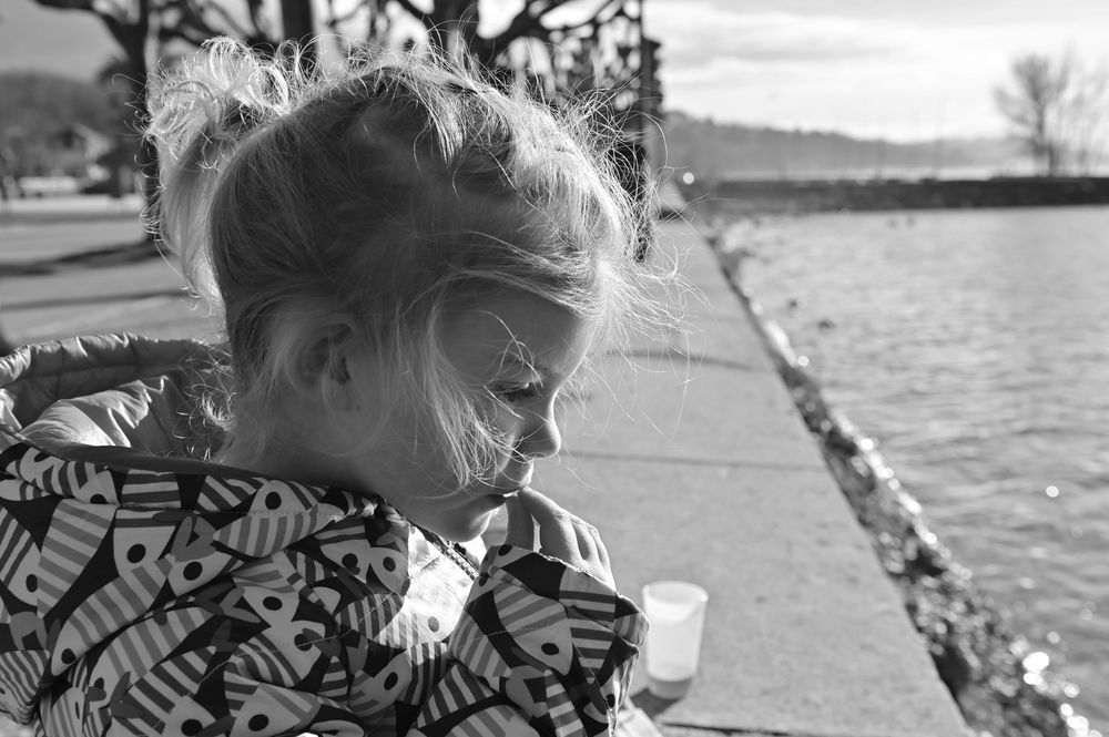 Portrait en noir et blanc d’un enfant au bord d’un lac avec montagnes en arrière-plan, ambiance naturelle et douce.