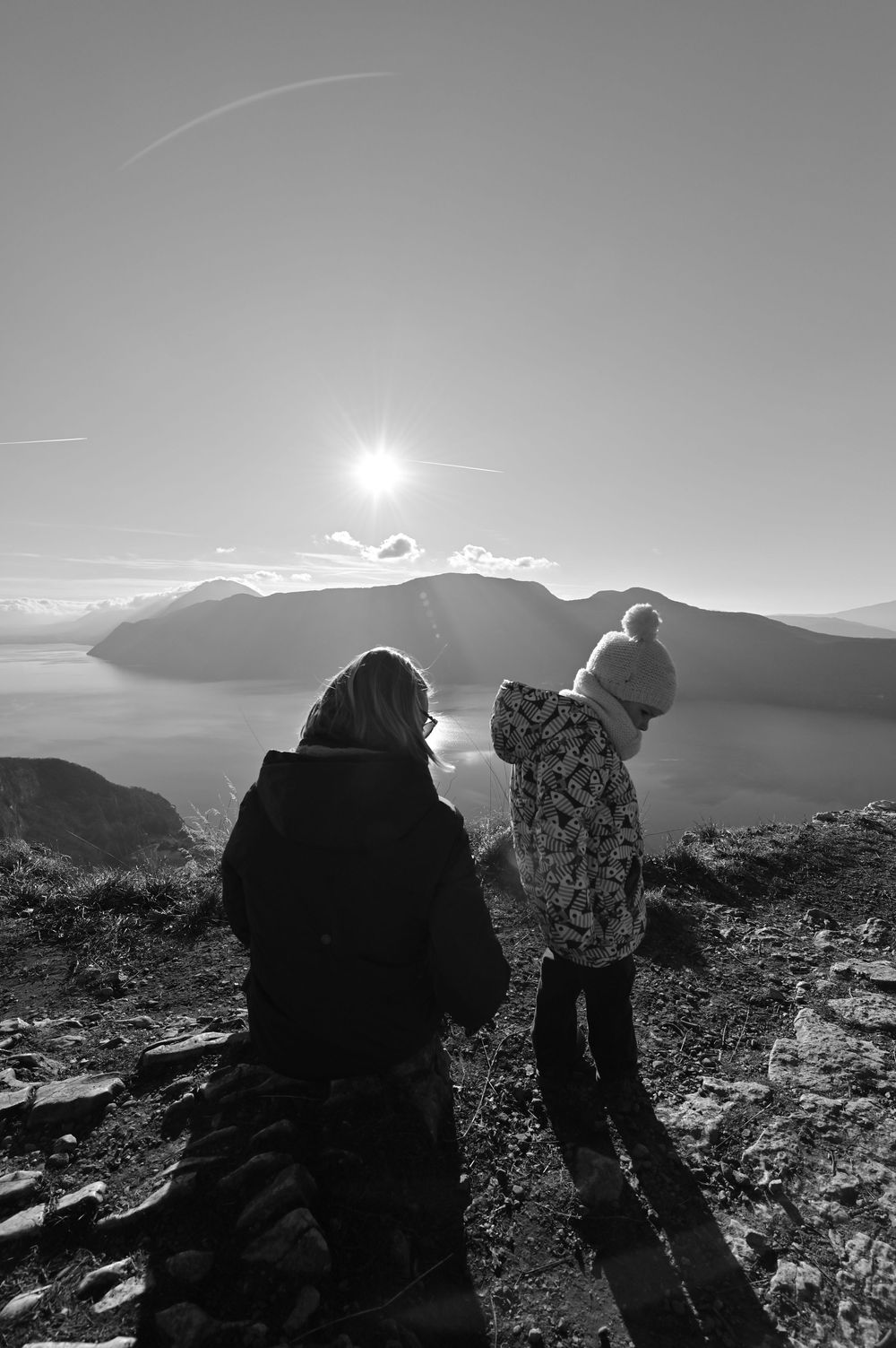 Silhouettes de personnes sur un sommet rocheux au coucher du soleil, paysage montagneux en noir et blanc.