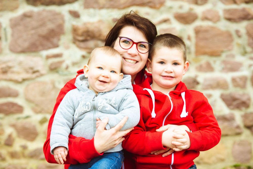 Portrait de famille souriant devant un mur en pierre en Bretagne, séance photo famille naturelle en extérieur.