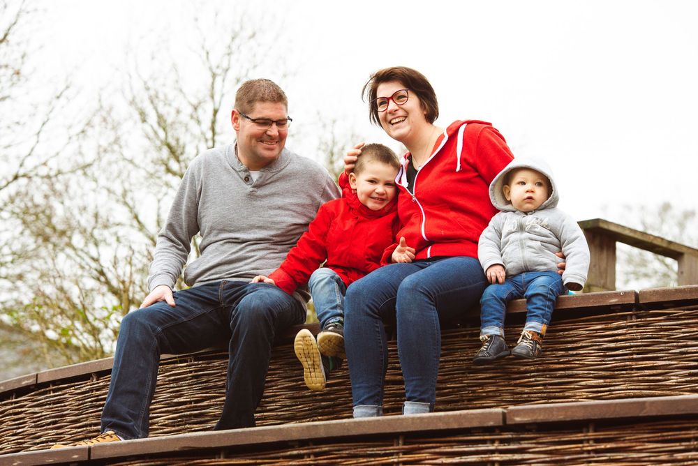 Famille assise sur une barrière en bois en extérieur en Bretagne, séance photo famille spontanée et authentique.