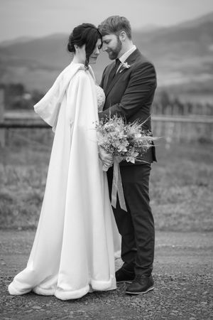 Black and white wedding photo of a couple in a romantic pose outdoors with mountains in background and bridal bouquet.