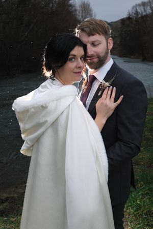 A couple shares an intimate moment outdoors while smoking cigarettes, with the bride wearing a white wrap.