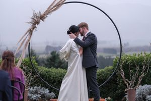 A couple shares a romantic moment under a circular floral arch during an outdoor wedding ceremony.