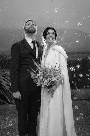 A black and white wedding photo showing a couple looking up at bubbles floating in the air while the bride holds a bouquet.