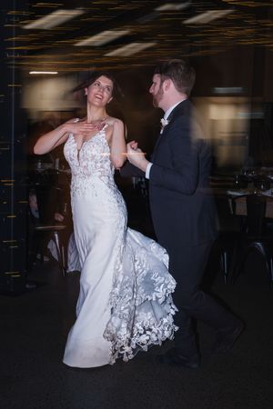 A couple dances together at a wedding reception, with the bride's white lace dress flowing gracefully during their movements.