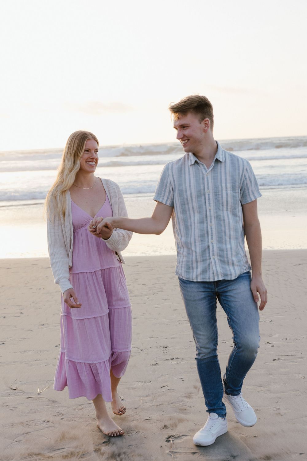 Happy couple walks hand in hand along the beach shore during a romantic sunset.