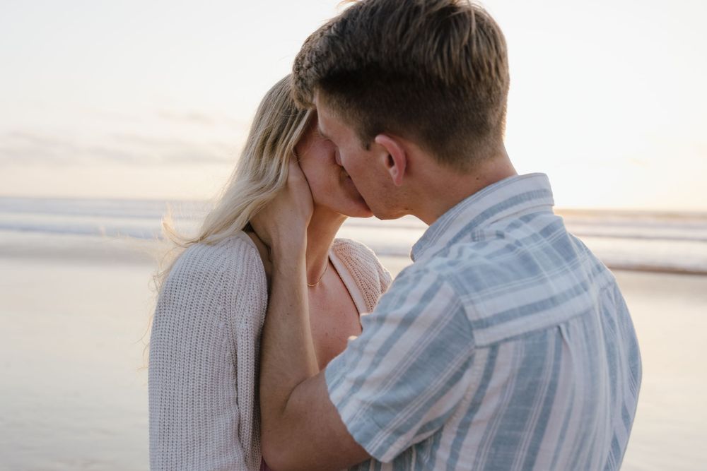 Romantic couple shares an intimate forehead kiss on the beach during a soft sunset.