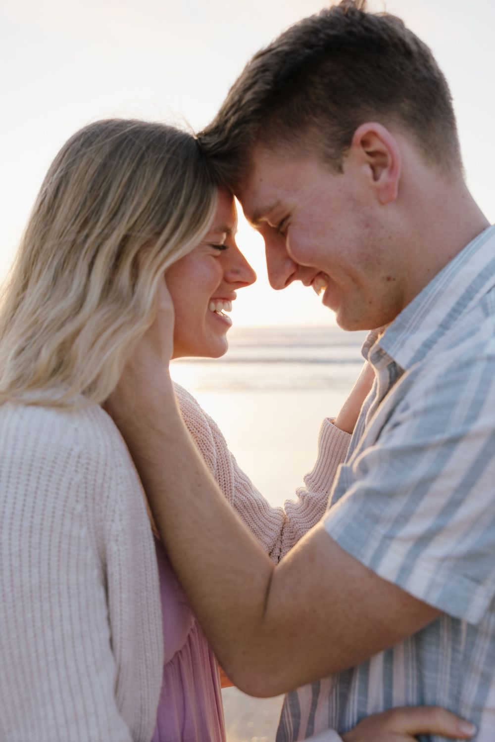 Happy couple touching foreheads and smiling at each other on a beach at sunset.