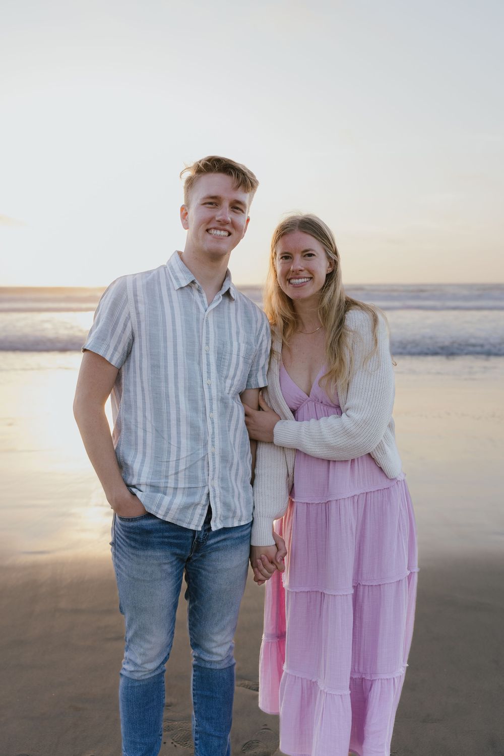 Smiling couple holding hands and posing together on a beach at sunset.