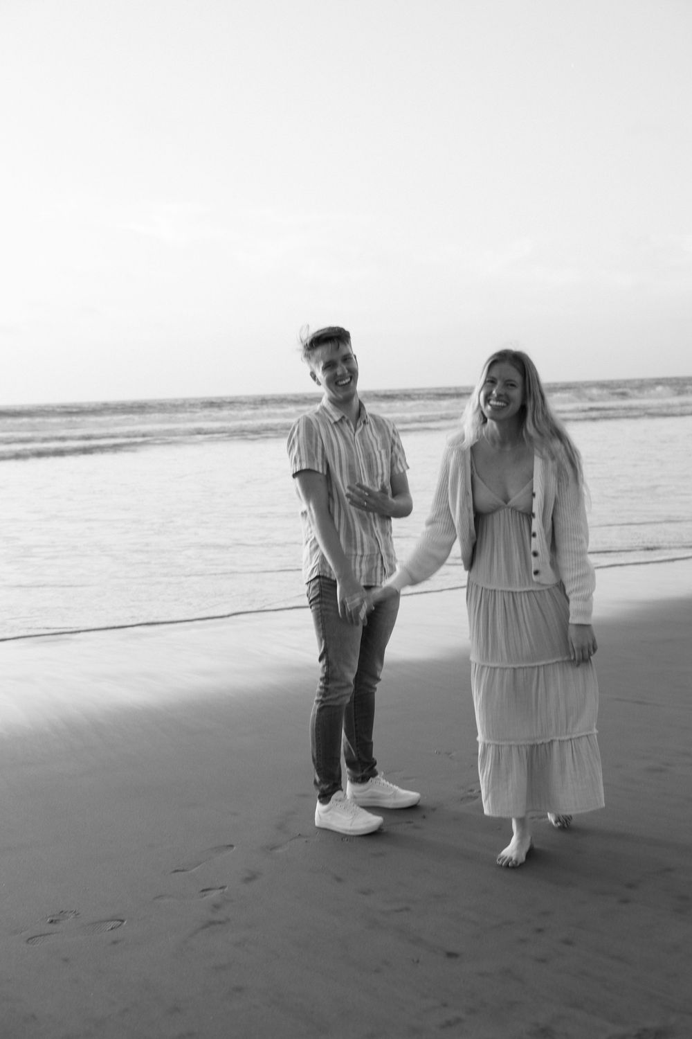 Black and white photo of happy couple holding hands and walking on a beach.