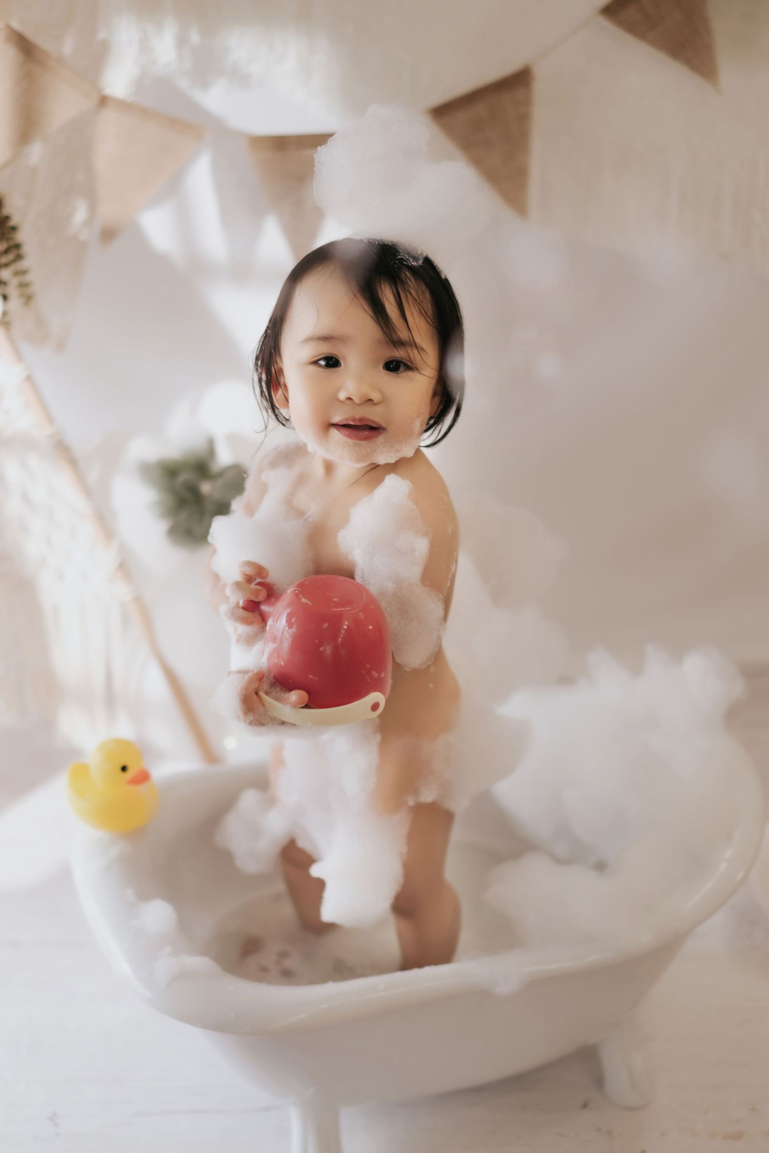 A baby cake smash photo session with white balloons, pampas grass, and rustic wood backdrop for first birthday celebration.
