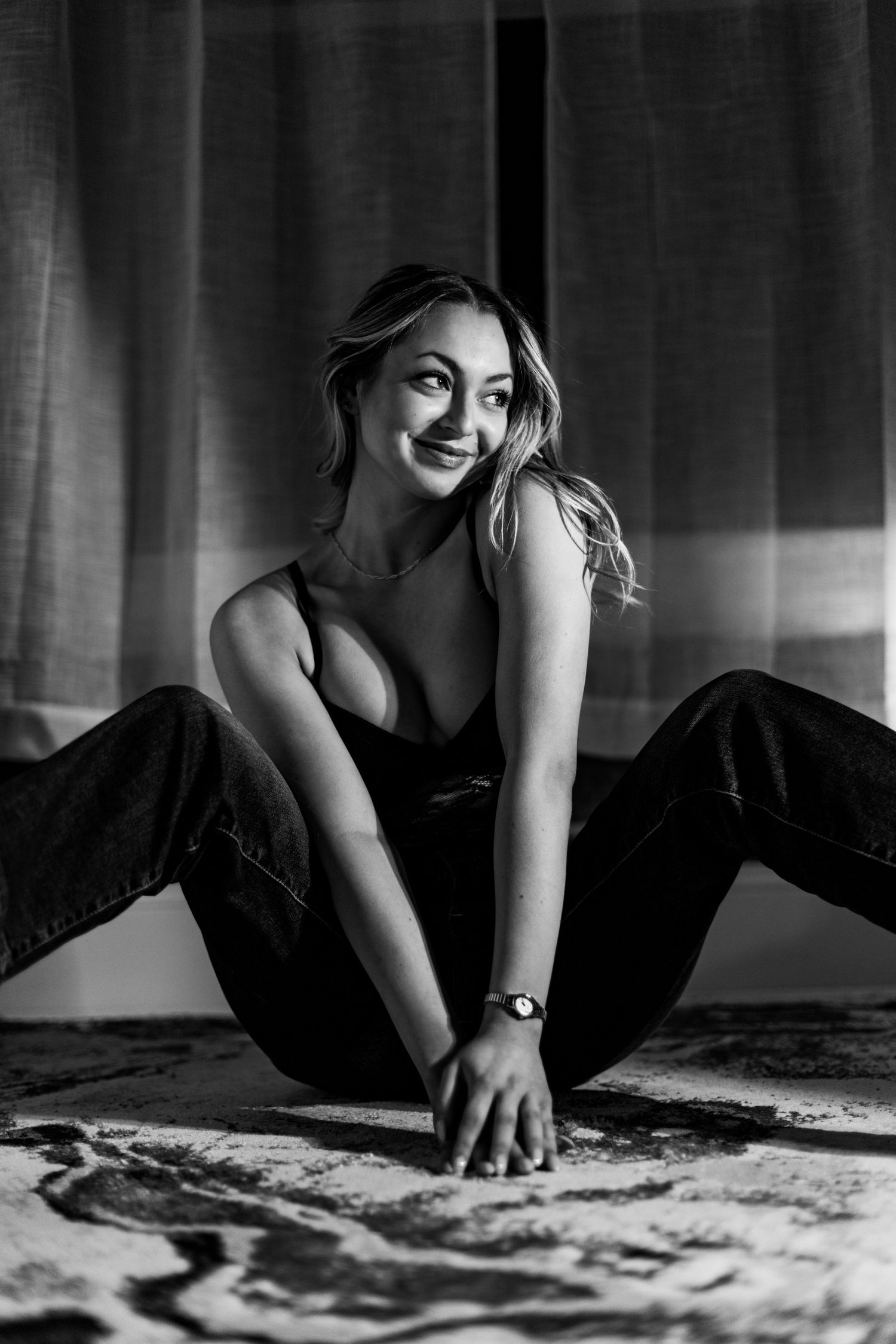 Black and white artistic portrait of someone sitting on the floor in casual attire with a joyful expression.