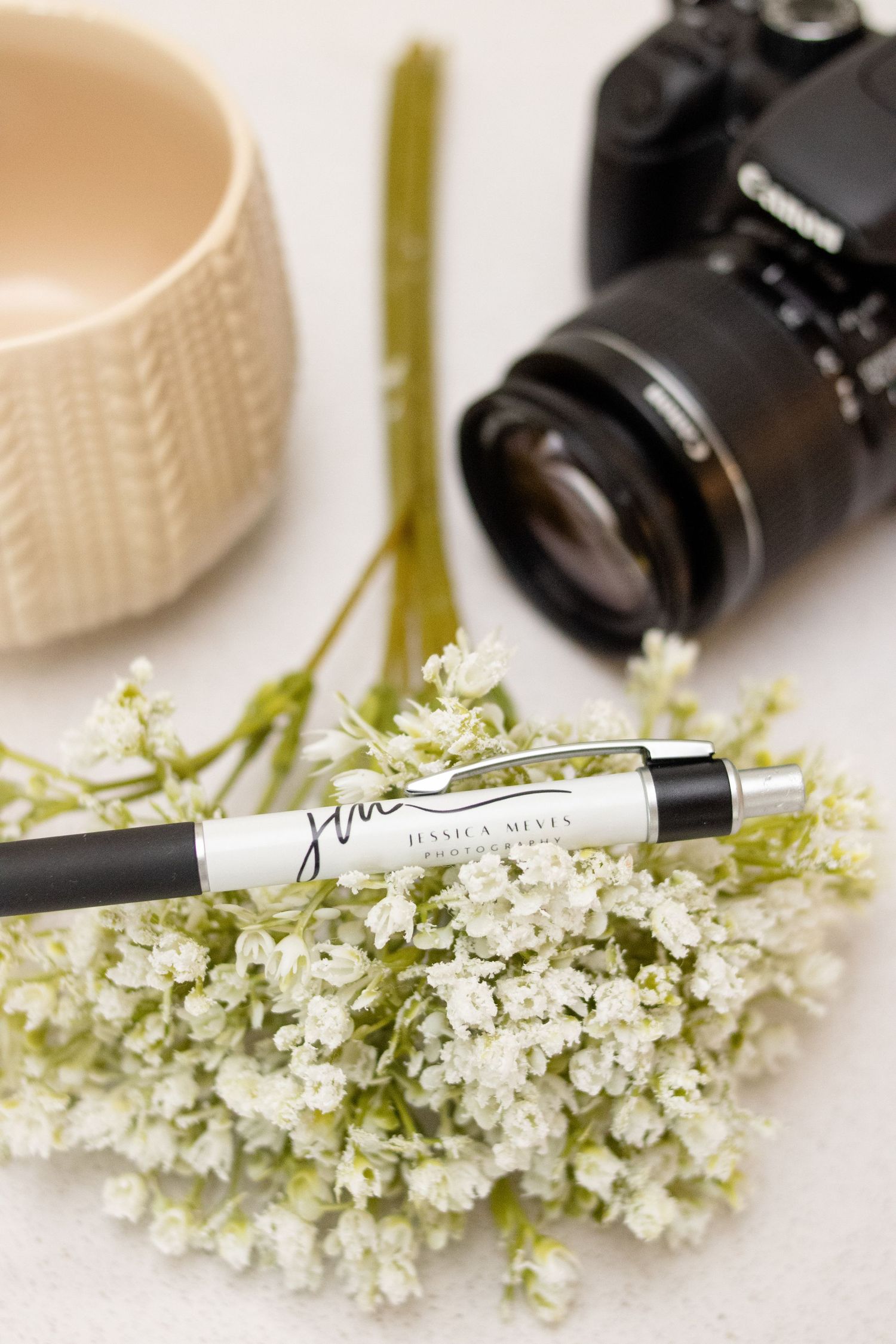Layout of professional camera, Jessica Meves Photography branded pen and other decor on a countertop.