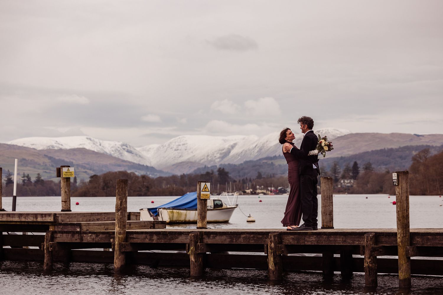 A panoramic sequence of people standing on a wooden pier overlooking snow-capped mountains and a serene lake.
