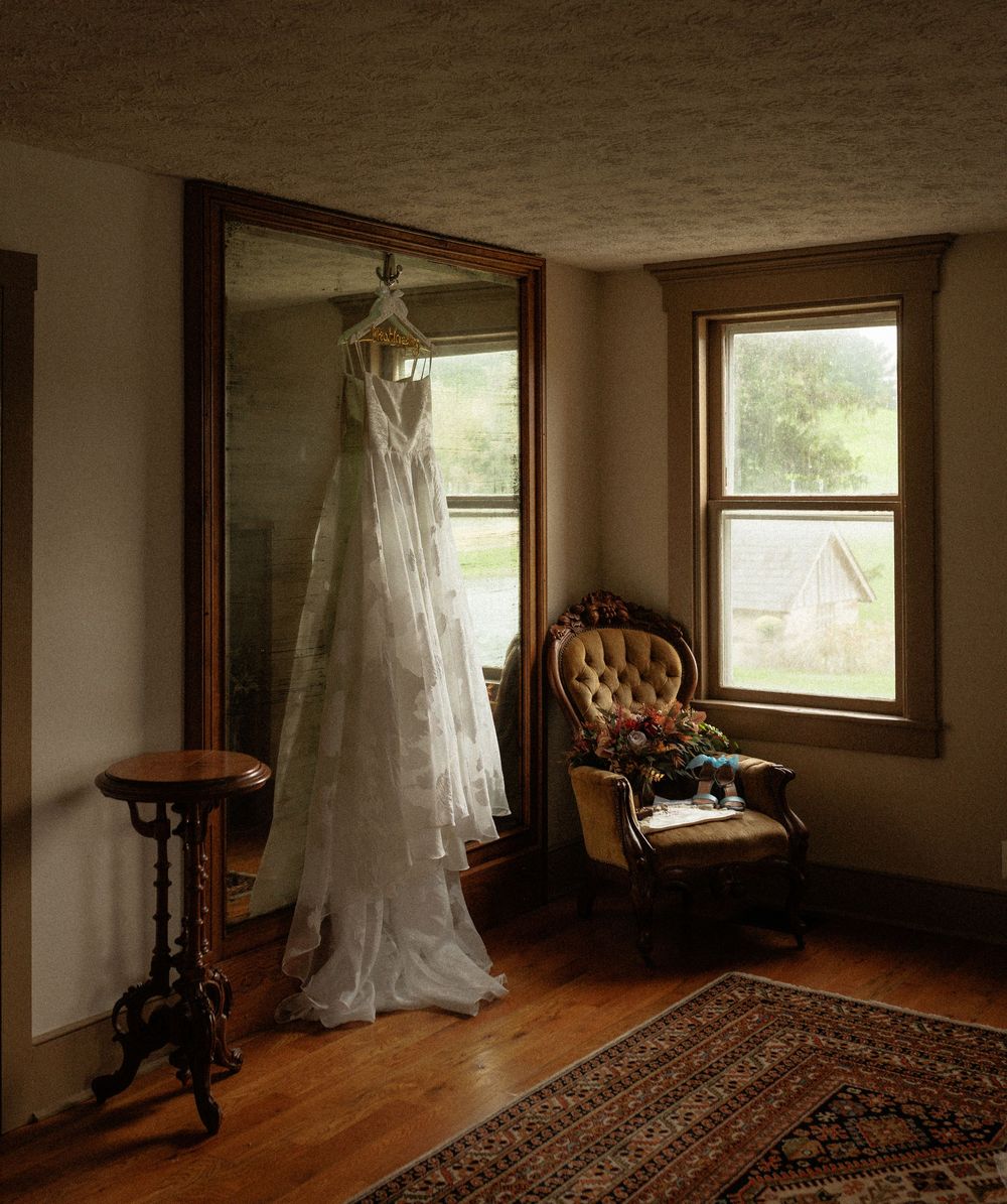 A wedding dress hangs elegantly in a sunlit room with hardwood floors and a vintage area rug.