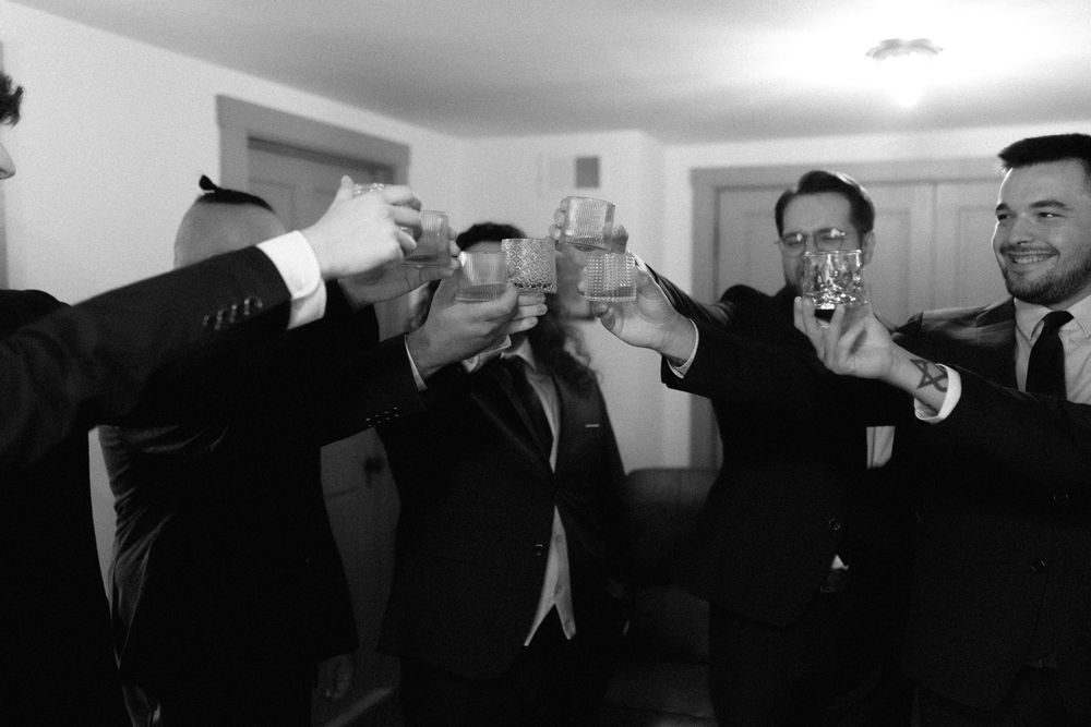 A black and white photo of groomsmen toasting with drinks at a wedding celebration.