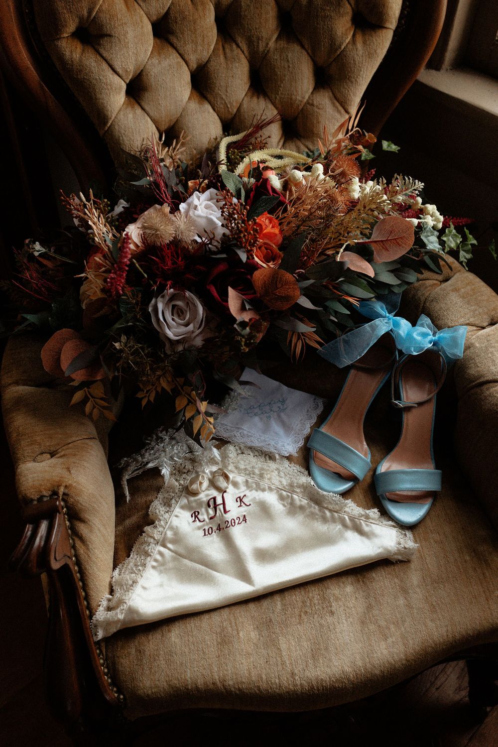 Wedding details including a vintage tufted chair with blue heels and autumn-toned floral bouquet.