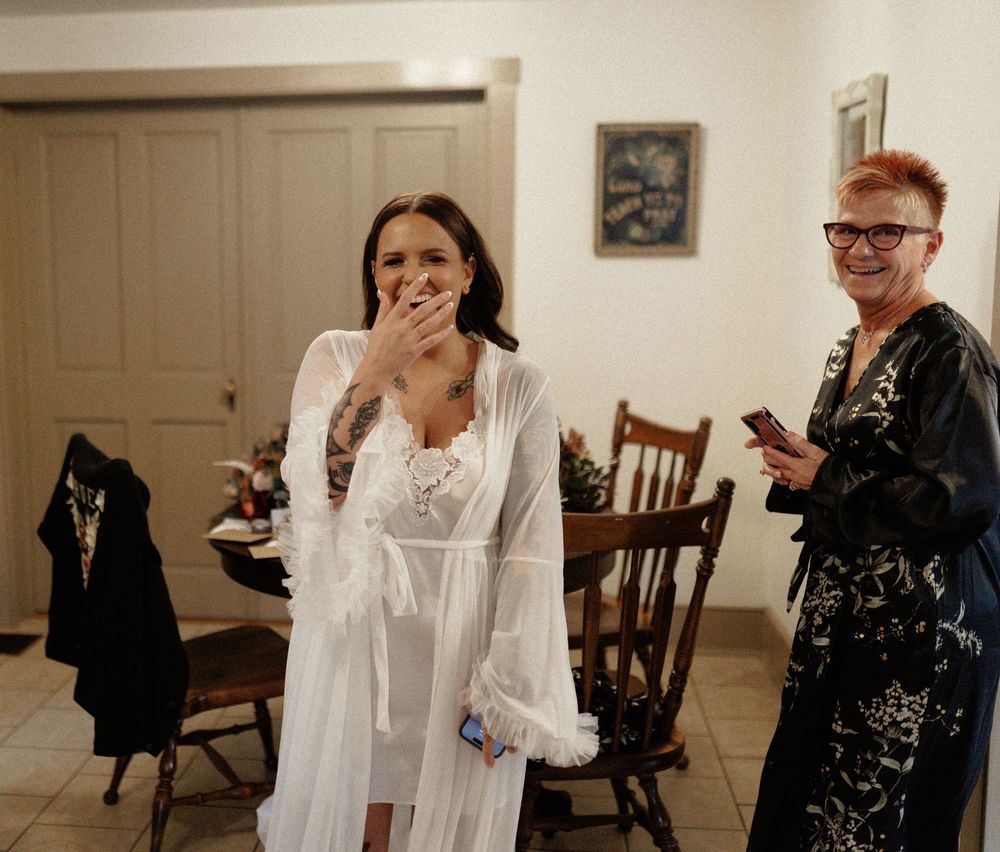 Two people share a candid moment in a home interior with wooden chairs and a door in the background.