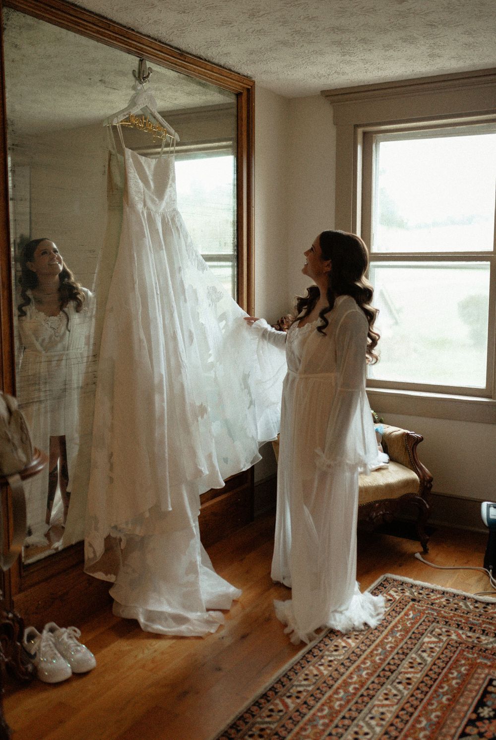 White wedding dresses hang in a room with hardwood floors and an oriental rug.