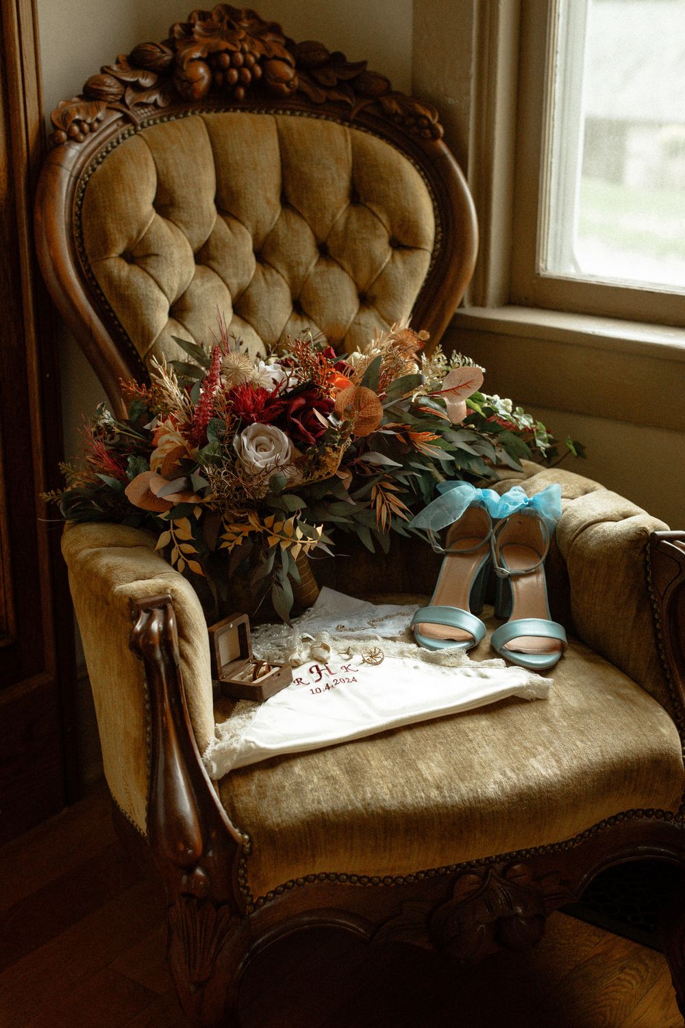 Vintage tufted settee with wedding shoes and floral arrangements by a window.