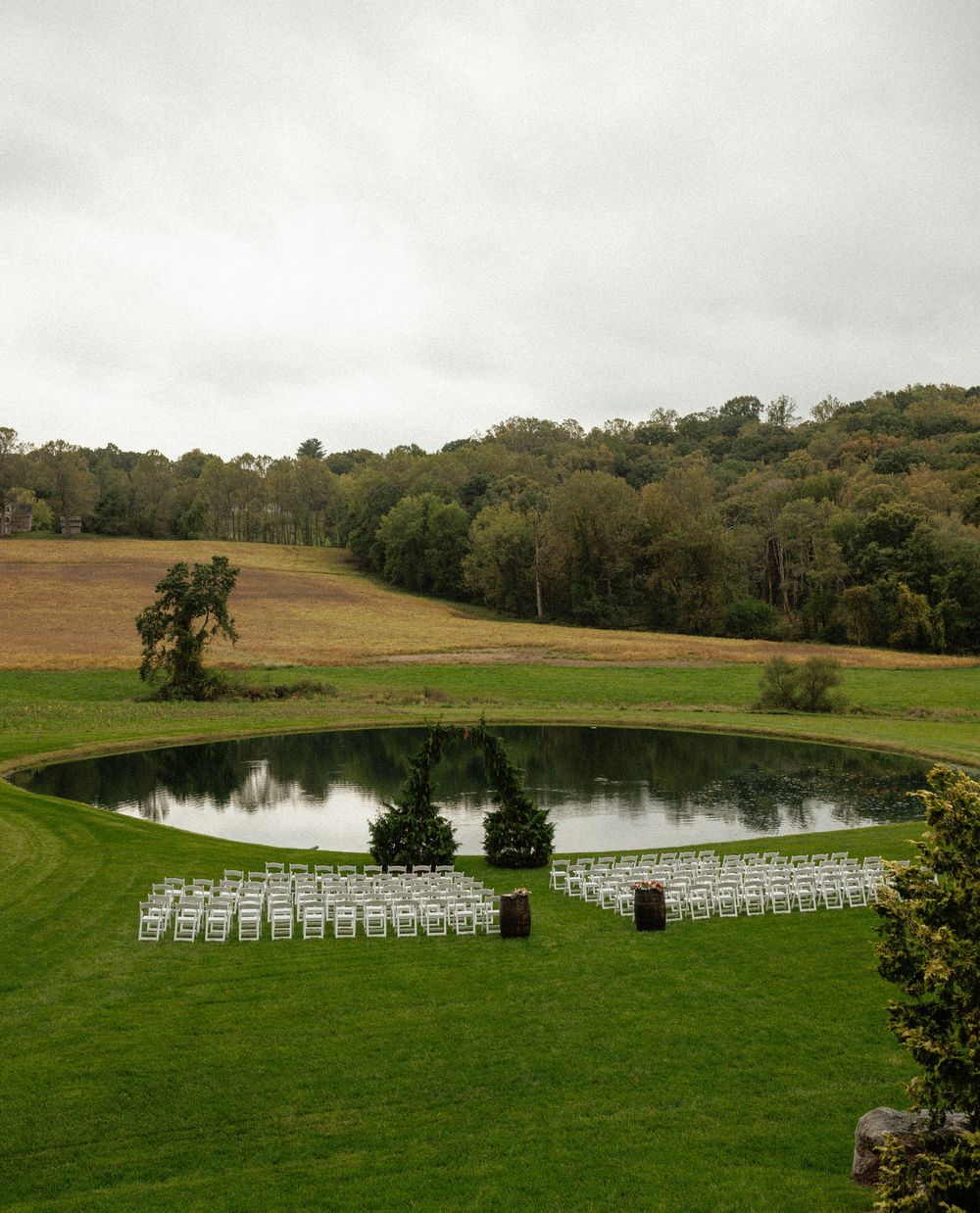 White chairs arranged in rows for an outdoor wedding ceremony beside a scenic pond.