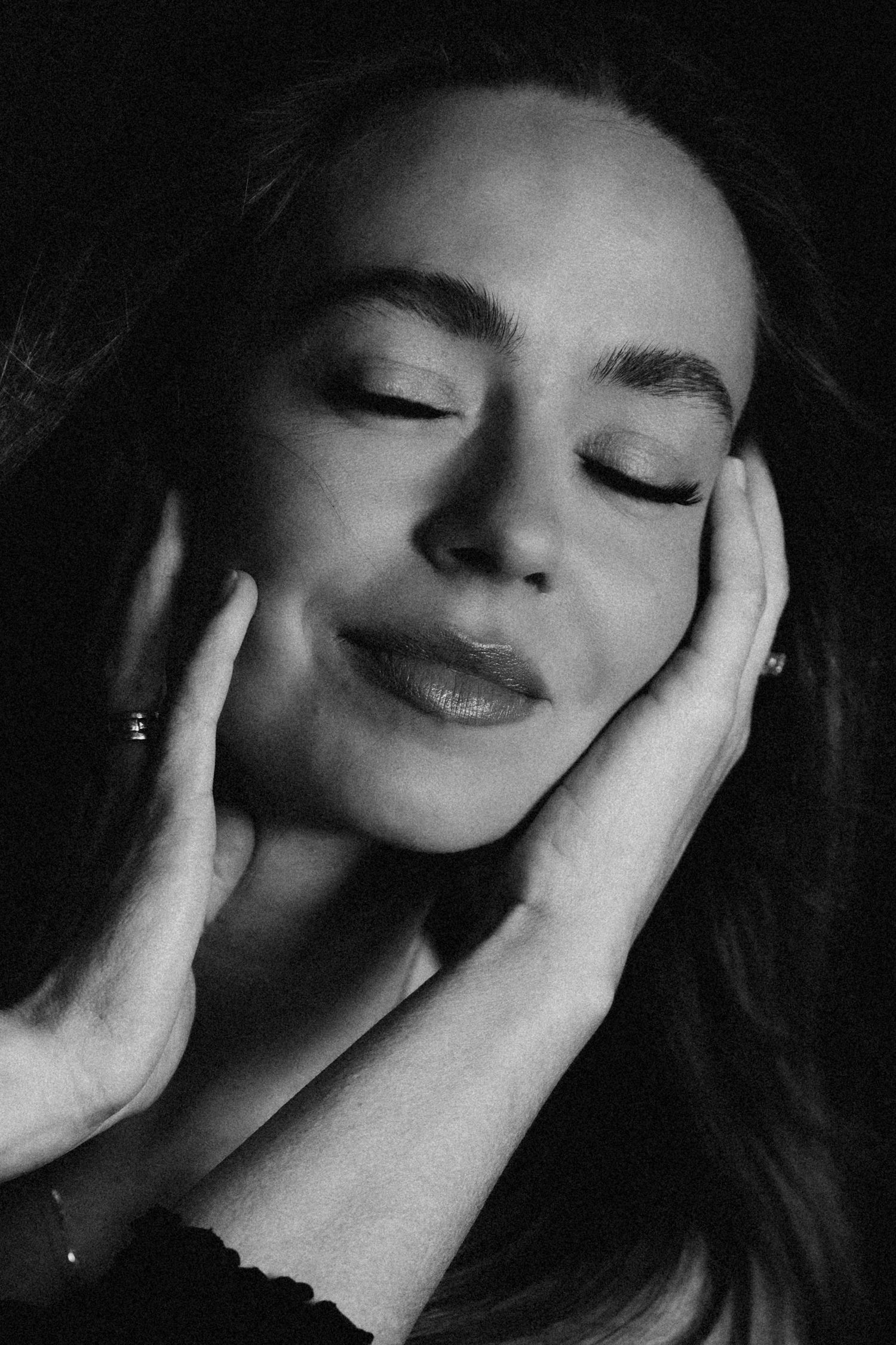 Black and white close-up portrait of a woman with closed eyes and hands gently cradling her face.