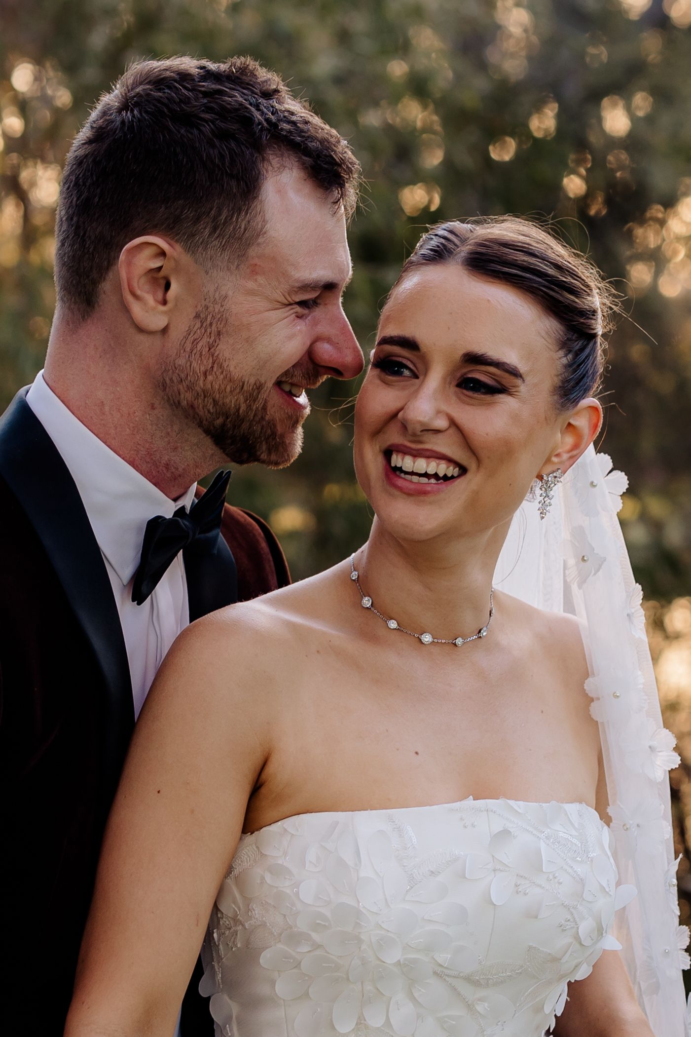 A joyful wedding couple shares an intimate moment outdoors with beautiful bokeh lighting in the background.