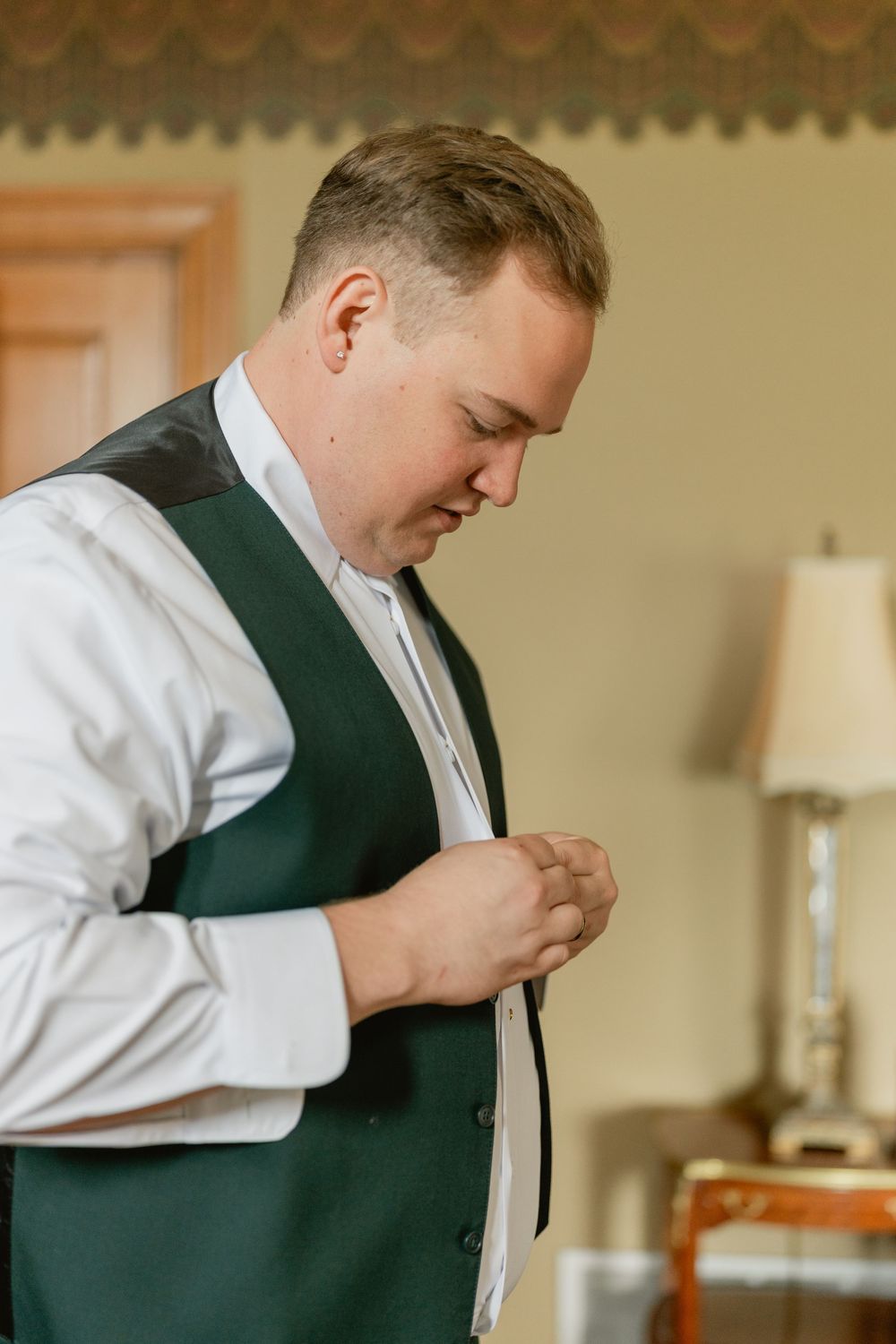 Person adjusts formal attire while getting ready in a room with scalloped wall details.
