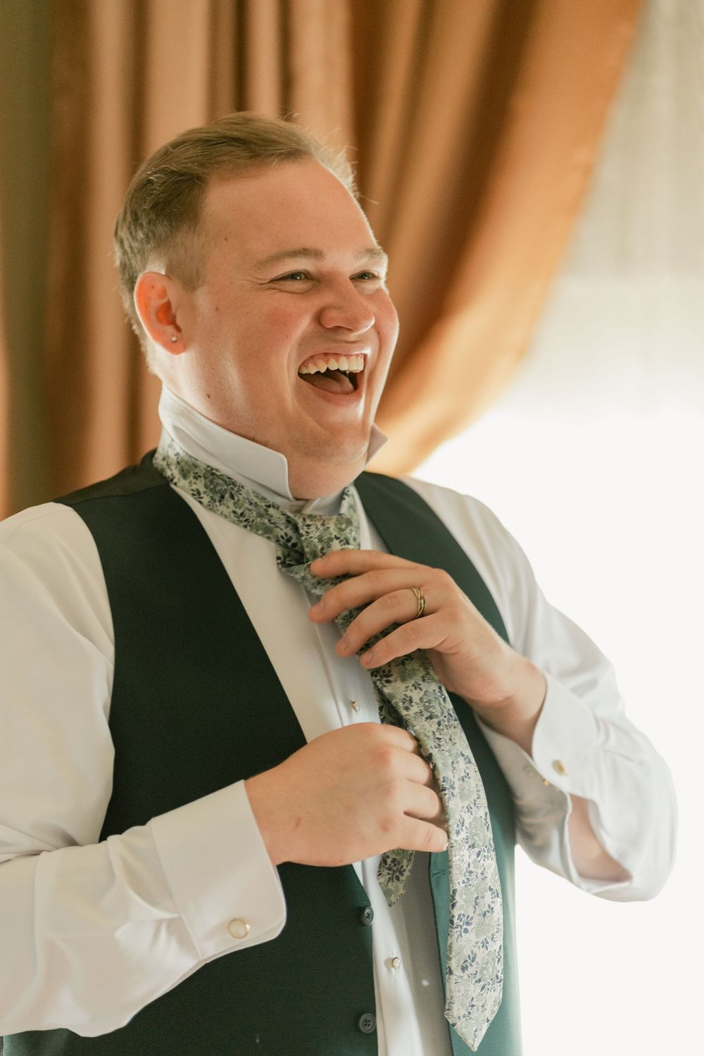 Candid sequence of a person adjusting their tie while laughing heartily during wedding preparations.