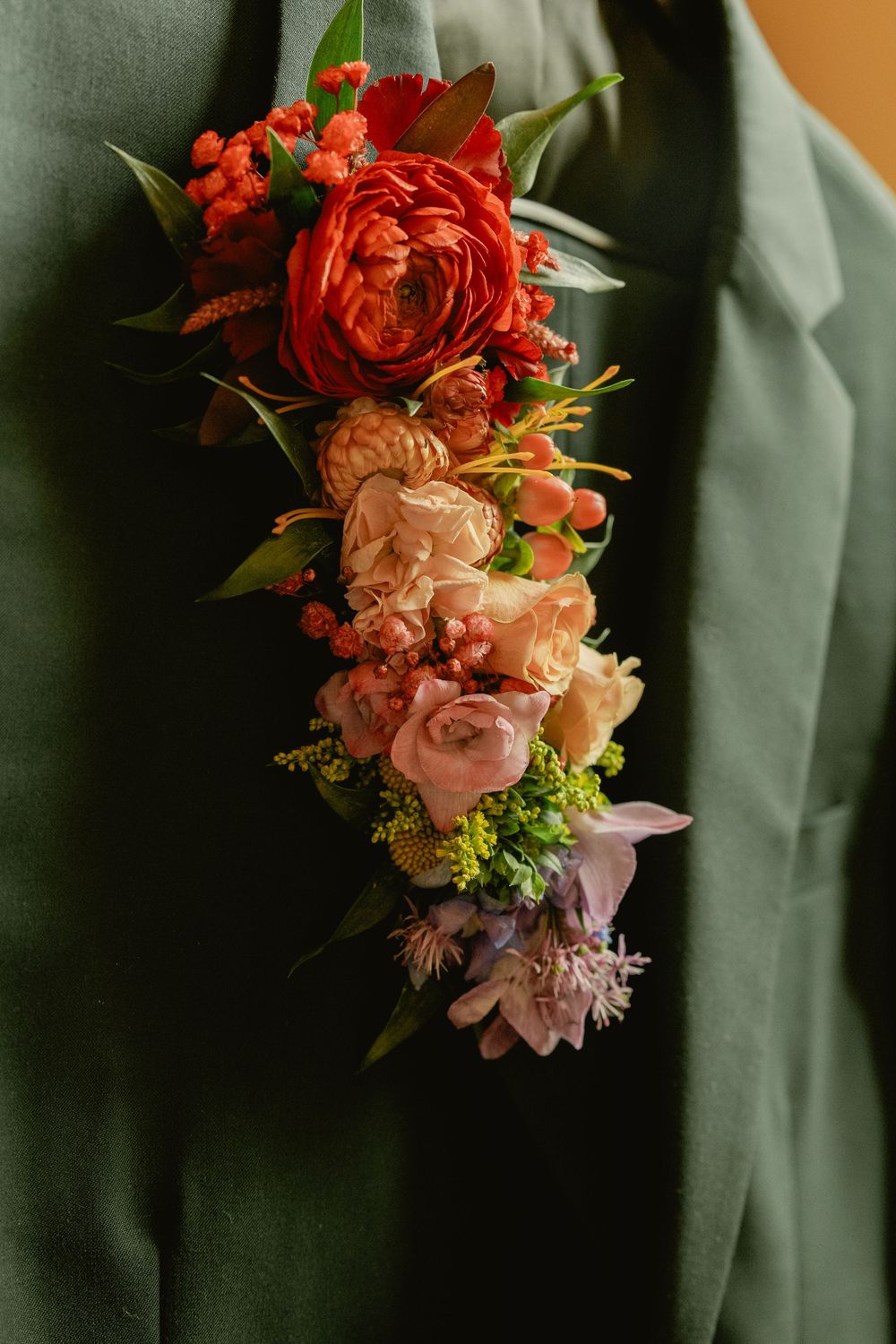 A row of pink and red floral boutonnieres pinned to green suit jackets at a formal event.