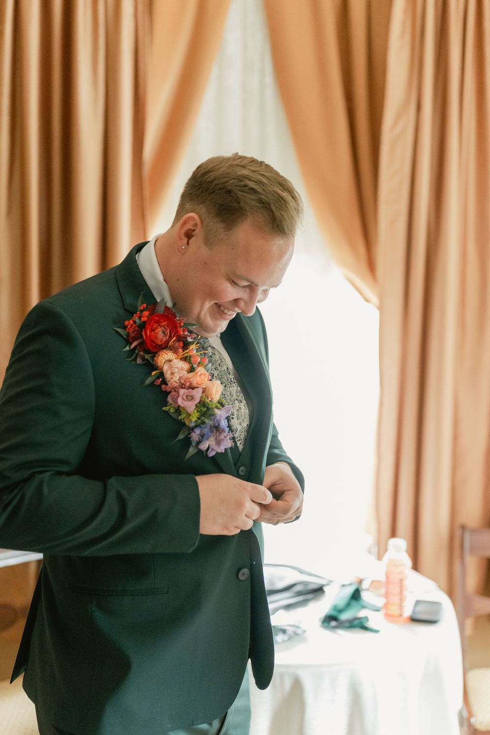 Person in a green suit jacket with colorful floral boutonniere adjusting their attire.