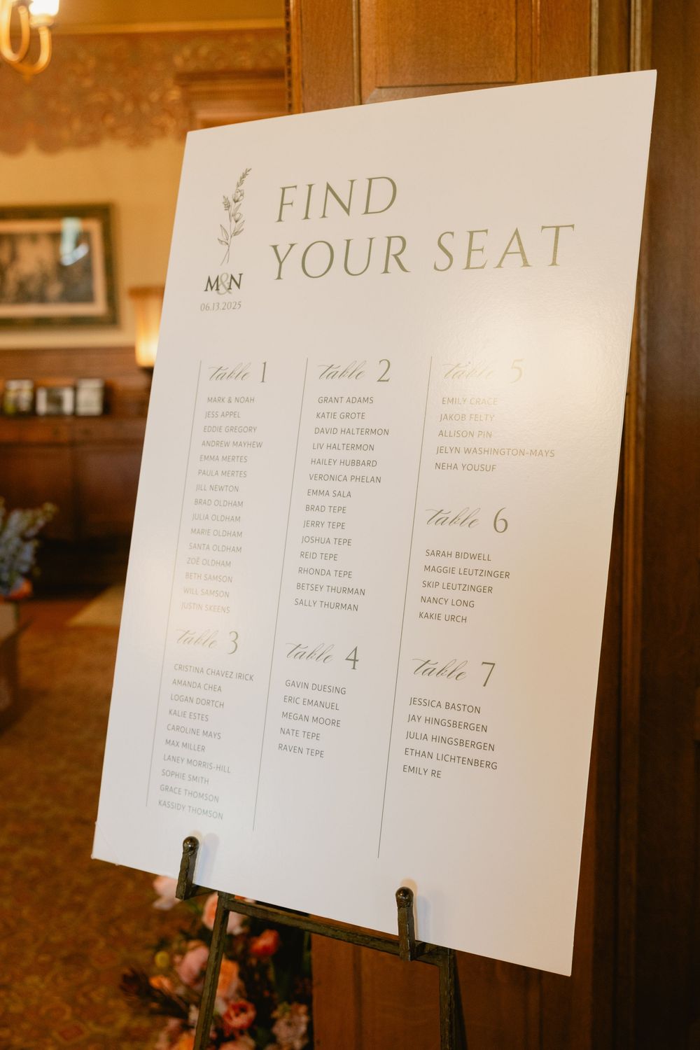 Wedding seating chart displays with table assignments posted on a wooden wall.