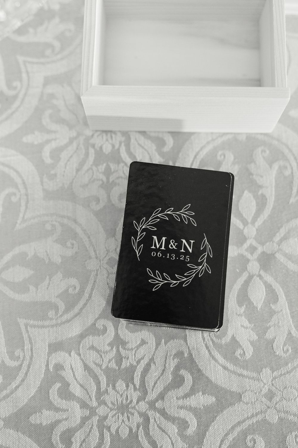 Black ring boxes with elegant monogram designs and wedding dates displayed on patterned background.