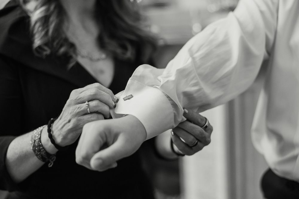 Black and white image showing hands adjusting a formal white dress shirt cuff with a bracelet visible.