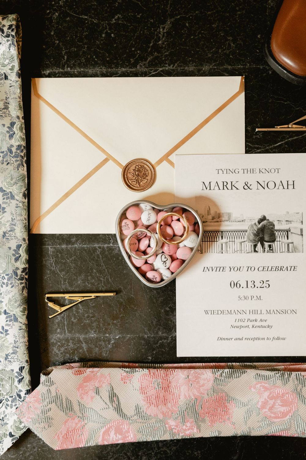Elegant wedding invitations with pink floral designs and wax seals displayed on a dark surface.