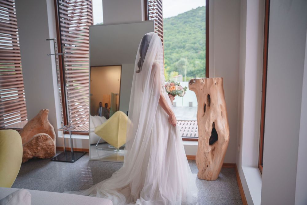 A flowing white wedding dress hangs by a window with mountain views and decorative wooden elements in the room.