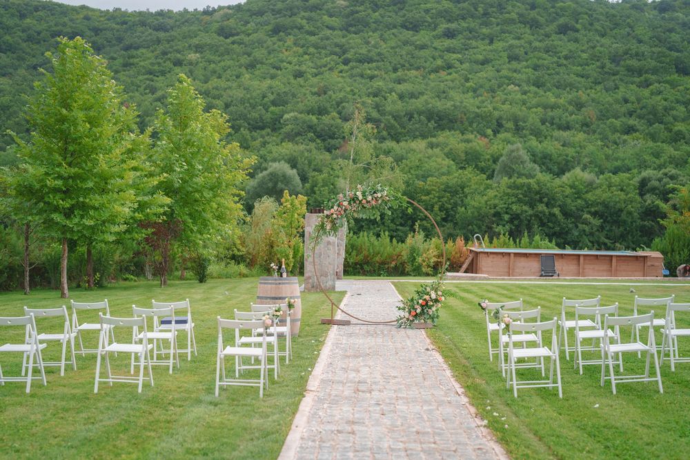 White chairs line a stone pathway leading to a wedding ceremony site with lush green mountains in the background.