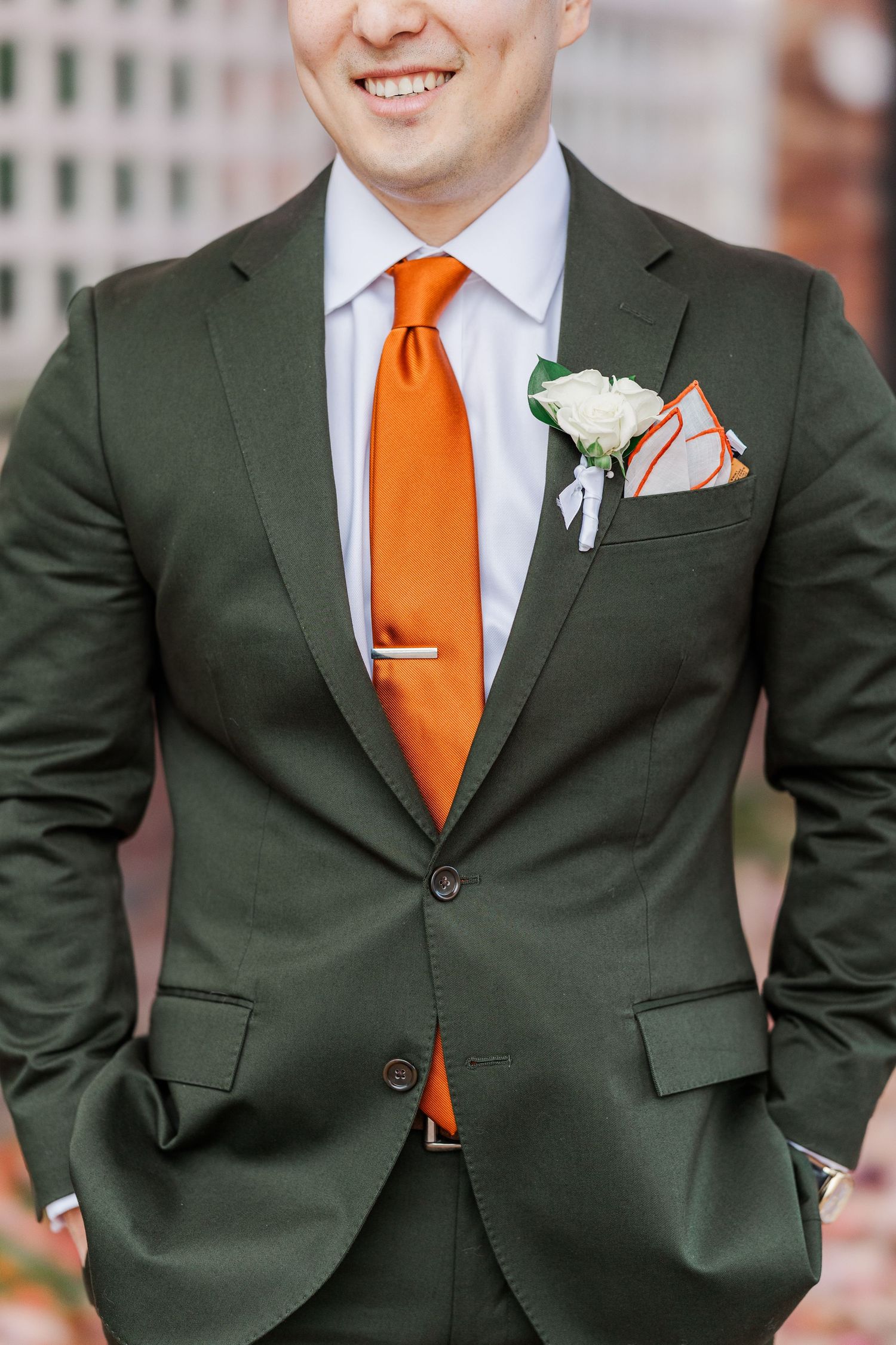 Wedding party members wearing dark green suits with bright orange ties and white boutonnieres stand together.