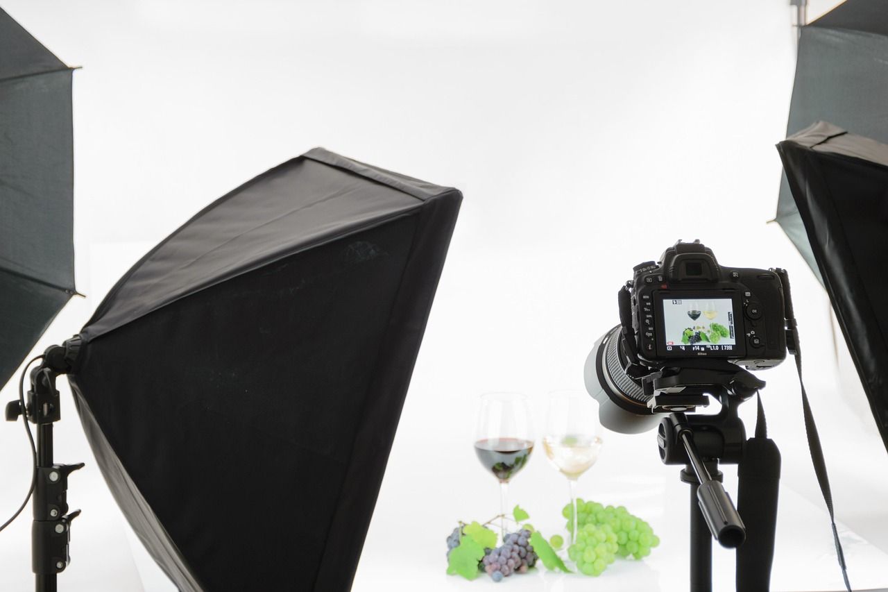 Set de fotografía profesional con softbox y cámara DSLR capturando copas de vino sobre fondo blanco.